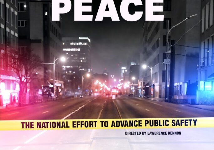 A city street at night with bright lights and a banner promoting peace and public safety.